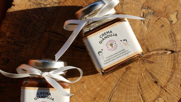Vasetti di crema gianduja da 95g, decorati con fiocchi bianchi e disposti su un tagliere in tronco di legno.