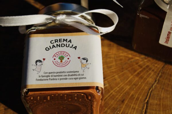 Vasetti di crema gianduja da 95g, decorati con fiocchi bianchi e disposti su un tagliere in tronco di legno.